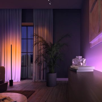 Soft ambient colored lighting in a modern living room with sheer curtains, a potted plant, and decorative objects on a cabinet.