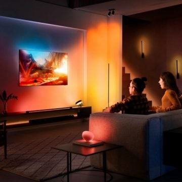 Two people sit on a sofa watching TV in a living room, with colorful smart lighting syncing to the screen content.