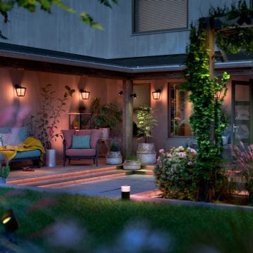 Outdoor patio with smart lighting creating a soft ambient glow, featuring seating, potted plants, and a garden area in the evening.