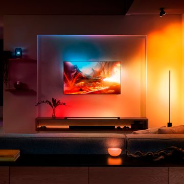 Wall-mounted television with smart lighting devices casting colored light effects on the wall, shelf, and table in a living room.