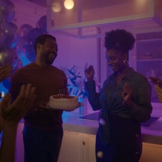 Group celebrating in a kitchen with balloons, cake and candles, enhanced by colorful smart lighting for a festive atmosphere.
