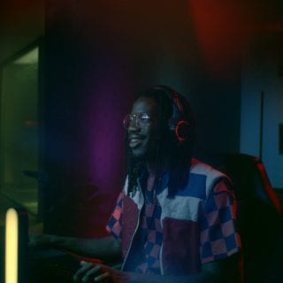 Person wearing headphones gaming at a desk, surrounded by colorful smart lighting in a modern entertainment room.