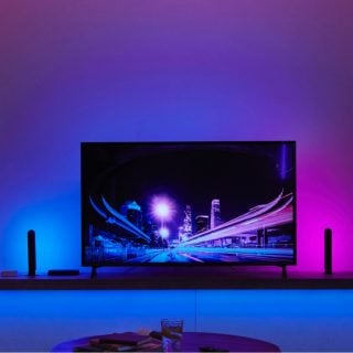 A television on a stand with two vertical smart light bars on each side, casting blue and pink light onto the wall behind.