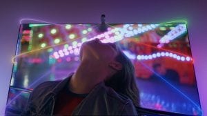 A living room entertainment setup with Philips Hue Play floor and table lamps either side of a TV and synced with the screen to create purple, orange, and pink wall washing effects. 