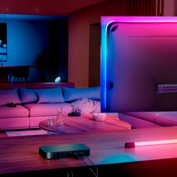 Flexible lightstrip attached to the back of a monitor displays gradient colors, illuminating the wall and desk in a gaming setup.