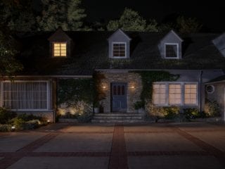 Outdoor smart lights mounted beside a front door illuminate the entrance and pathway, highlighting the steps and nearby plants.
