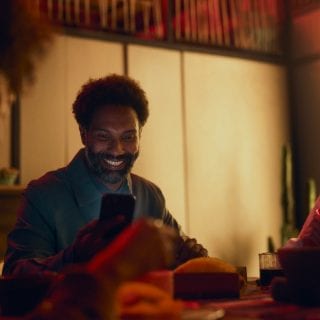 A group of people seated at a dining table, illuminated by warm smart lighting, with one person using a smartphone indoors.
