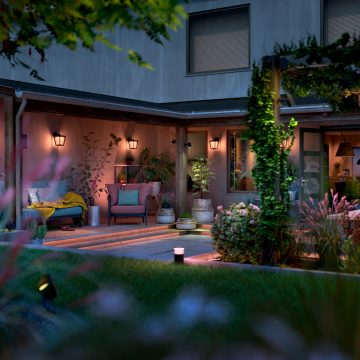 Outdoor wall lights and pathway lights illuminate a covered patio area with seating and plants, providing functional driveway lighting.