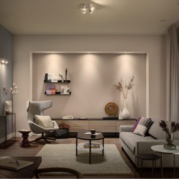 Ceiling-mounted white ambiance bulbs illuminate a modern living room, highlighting shelves and furniture with even, soft light.