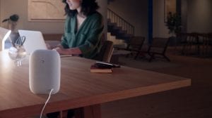 Person working at a desk in a modern living space, illuminated by a smart desk lamp, with a smart speaker in the foreground.