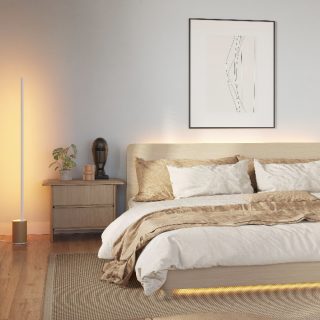 Tall smart floor lamp placed beside a bed, casting adjustable white light onto the wall and floor in a modern bedroom.