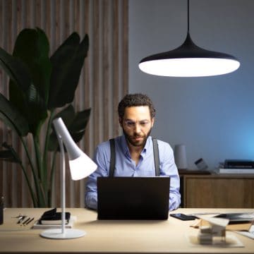 Pria yang duduk di depan laptop di meja dengan dua lampu pintar