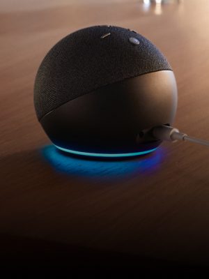 A spherical smart speaker with fabric top sits on a wooden surface, emitting a blue light ring at its base while connected by cable.