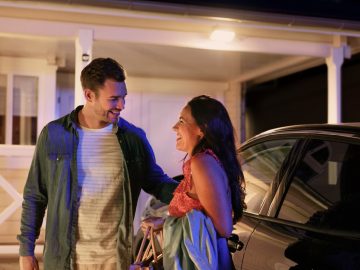 Two people standing next to a car in a driveway at night, illuminated by outdoor smart lighting near a house entrance.