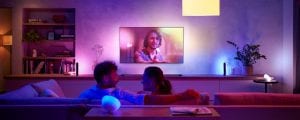 A group of people watching TV in a living room with colorful smart lighting synced to the screen content.