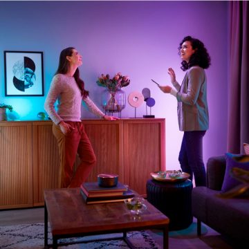 Two people in a living room setting interact near a sideboard, surrounded by colorful smart lighting and modern decor.