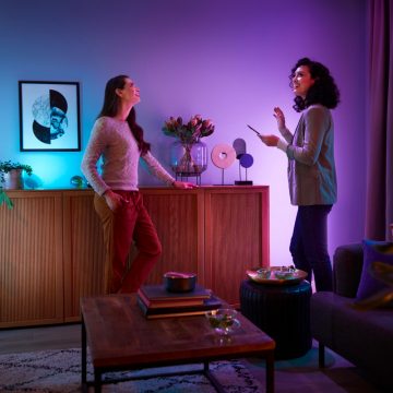 Two people in a living room are conversing, illuminated by colorful smart lighting that highlights the modern decor and artwork.