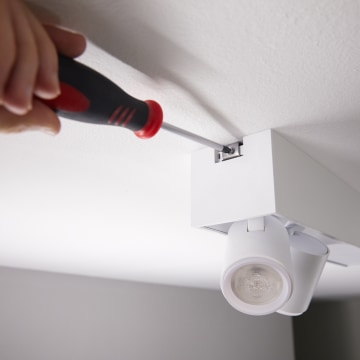 Hand using a screwdriver to install or secure a white ceiling-mounted smart track light fixture.