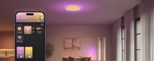 A smartphone displays a lighting control app with scenes like ""Spring custom"" and controls for Datura backlight and panel. Ceiling light glows purple.