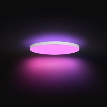 Round ceiling smart LED light emitting a uniform pink and purple glow, creating soft ambient lighting in a dark room.