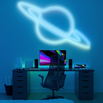 A Hue Essential flex strip light bent into the shape of a planet mounted above a desk with computer and glowing in white and pale blue light. 