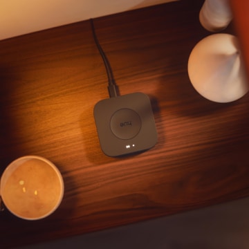 A Hue Bridge Pro smart home hub in black placed on a wooden table. 