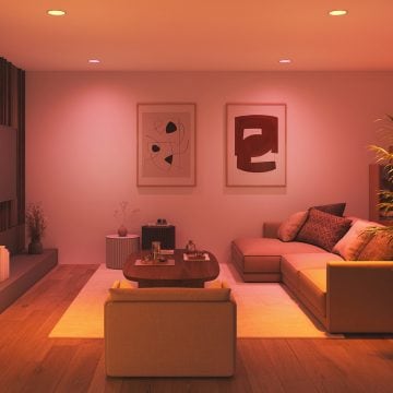 A living room space lit in warm tones of pink and white smart light.
