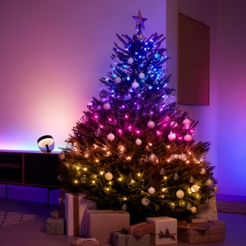 Christmas tree decorated with multicolored smart lights and ornaments in a living room, creating a soft ambient glow.