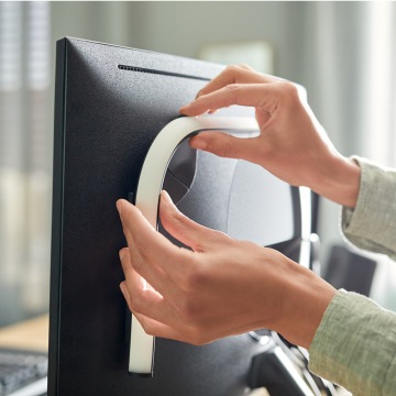 Hands attaching a flexible light strip to the back of a computer monitor, demonstrating easy installation of smart lighting.