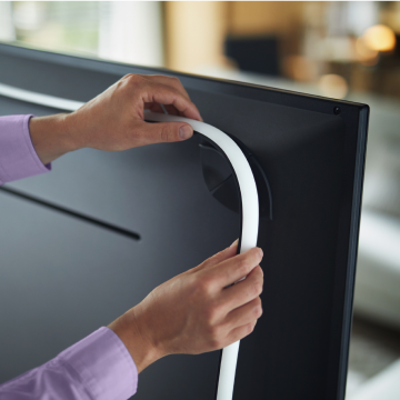 Hands attaching a flexible lightstrip to the back of a television, securing the strip along the edge for ambient lighting.
