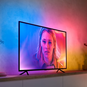 Television on a cabinet in a living room with gradient colored ambient light softly illuminating the wall behind the screen.