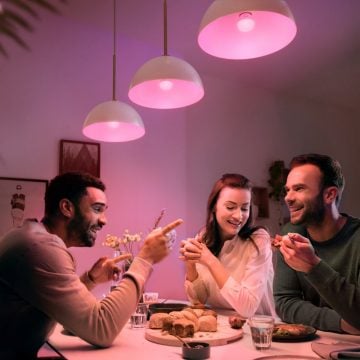 A group of people sharing a meal at a dining table under pendant lights with a pink hue, enhancing the dining room setting.