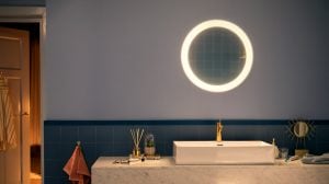 Round illuminated bathroom mirror mounted above a sink, casting bright light onto the countertop and surrounding fixtures.