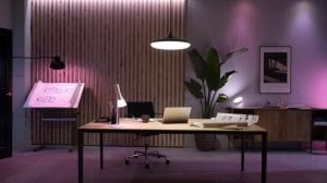 Desk lamp and pendant light illuminate a home office desk with smart lighting, casting white and colored light on work surfaces.