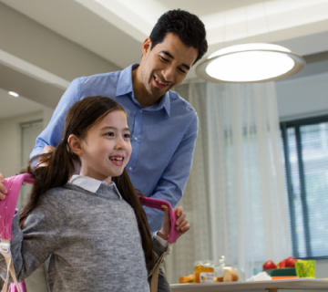 An adult helps a child with a backpack in a modern dining area, illuminated by a round ceiling smart light above the table.