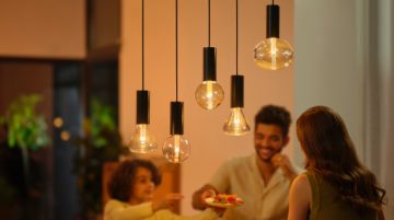 A group of people gathered in a warmly lit dining area, with several hanging smart bulbs providing soft illumination above.