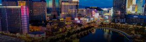 Las Vegas cityscape at dusk with illuminated buildings, vibrant signage, and soft ambient glow reflecting on water.