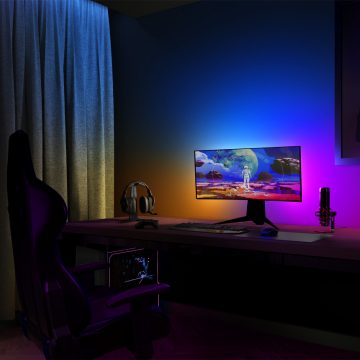 Curved monitor on desk with colored LED spotlights casting blue, orange, and purple light on wall behind computer setup.