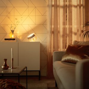 A smart table lamp with a translucent base is placed on a cabinet, casting warm light onto a geometric-patterned wall.