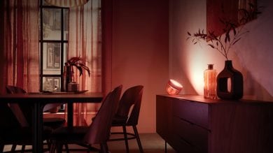 A smart table lamp placed on a sideboard, casting colored light onto the wall behind decorative vases and branches.