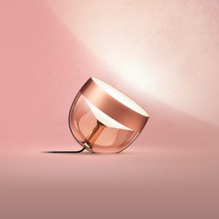 Copper Iris table lamp with rounded shape, glossy finish, clear base, and visible power cord placed on a flat surface.
