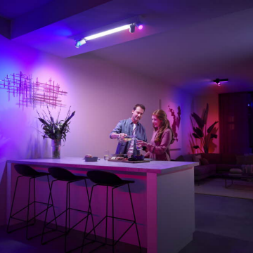 Two people preparing drinks at a kitchen island under colorful smart lighting, with purple and pink tones illuminating the modern space.