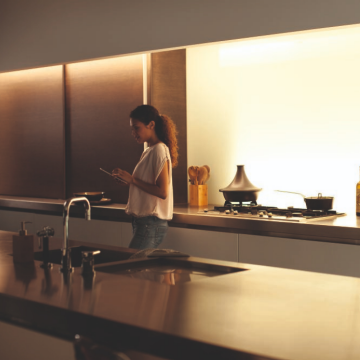Person using a tablet in a modern kitchen, illuminated by warm under-cabinet lighting above the stove and countertop.