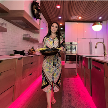 Person carrying a pan in a modern kitchen with colorful smart lighting illuminating the ceiling and floor.