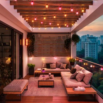 String lights emitting a soft ambient glow in warm colors decorate a modern balcony lounge with city views at sunset.