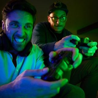 Two people playing video games with controllers in a living room, illuminated by colorful green and blue smart lighting.