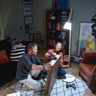Two people assembling furniture in a living room, illuminated by a tall smart floor lamp providing focused light on their activity.