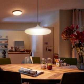 A pendant light fixture with a white smart bulb is suspended above a wooden dining table, casting bright illumination on the surface.