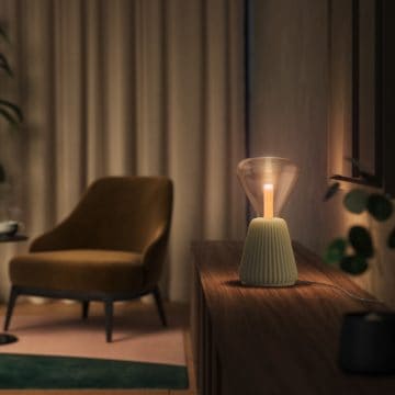 A table lamp with a ribbed base and glass shade is placed on a wooden surface, emitting light onto the wall and nearby objects.