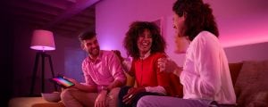 Group of people sitting on a sofa in a living room, using a tablet with pink smart lighting illuminating the space.